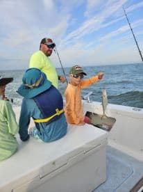 A young angler proudly displaying a caught fish while enjoying a fishing trip on a boat, surrounded by fellow young anglers.