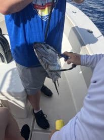 Two anglers on a boat handling a large fish, showcasing their catch during a deep-sea fishing trip.
