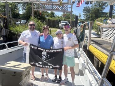 A cheerful group of anglers posing with a flag for 'Four Winds Chartering' on the deck of their boat, showcasing a fun day of fishing anticipation.