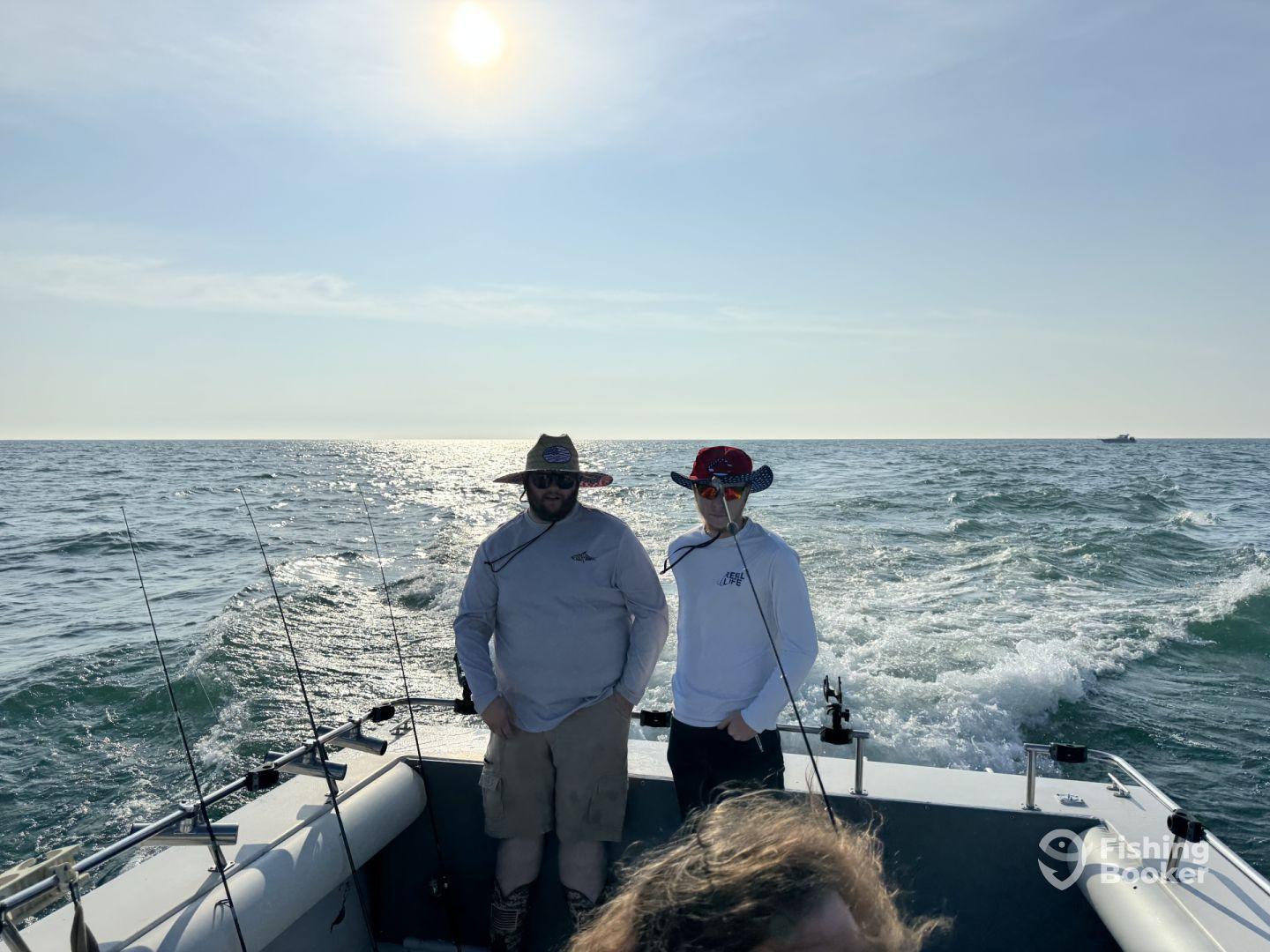 Two anglers enjoying a sunny day on the water aboard a fishing boat, with fishing rods ready for action.