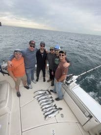A group of six anglers proudly displaying their catch of several Spanish Mackerel on the deck of a sportfishing boat during a successful offshore trip.