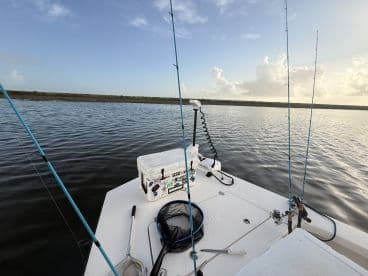 View of the boat's interior with fishing rods and a cooler, set against a serene water backdrop, ideal for a day of fishing.