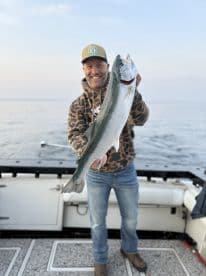 Angler proudly displaying a large Silver Salmon while fishing on a boat, showcasing a successful day on the water.