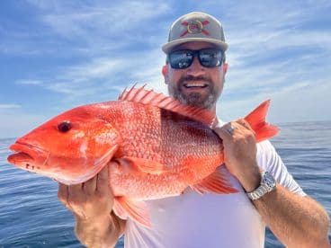 Angler proudly displaying a large Red Snapper while fishing offshore, showcasing a beautiful day on the water.