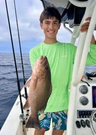 A young angler proudly displaying a large Snapper while fishing on a boat, showcasing the excitement of a successful catch.