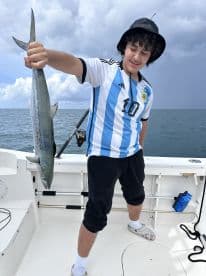 Young angler holding a Barracuda on a fishing boat, showcasing a successful catch during a deep-sea fishing trip.