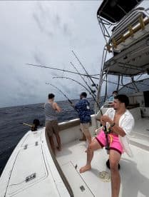 Group of anglers actively fishing on a sportfishing boat, with rods bent and lines in the water, showcasing an exciting day at sea.