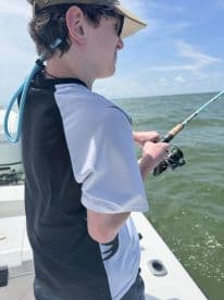 A young angler focused on reeling in a catch while fishing on a boat in open waters.