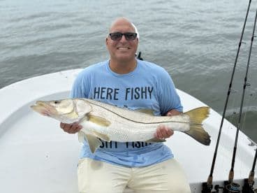 Angler proudly displaying a large Snook while seated on a boat, showcasing a successful fishing trip.