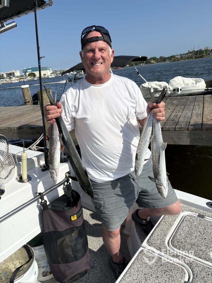 An angler proudly displaying two freshly caught Spanish Mackerel on a boat, enjoying a successful day of fishing.