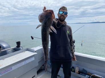 An angler proudly displaying a large Lingcod while fishing on a boat in calm waters.