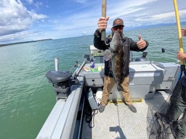 An angler proudly displaying a large Grouper while fishing from a boat in a scenic coastal environment.