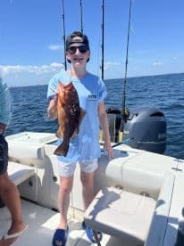 A young angler proudly displaying a large Grouper while fishing on a sunny day, showcasing the excitement of a successful catch.