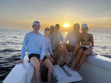 Group of young anglers enjoying a sunset on a boat, showcasing a relaxed atmosphere before their fishing adventure.