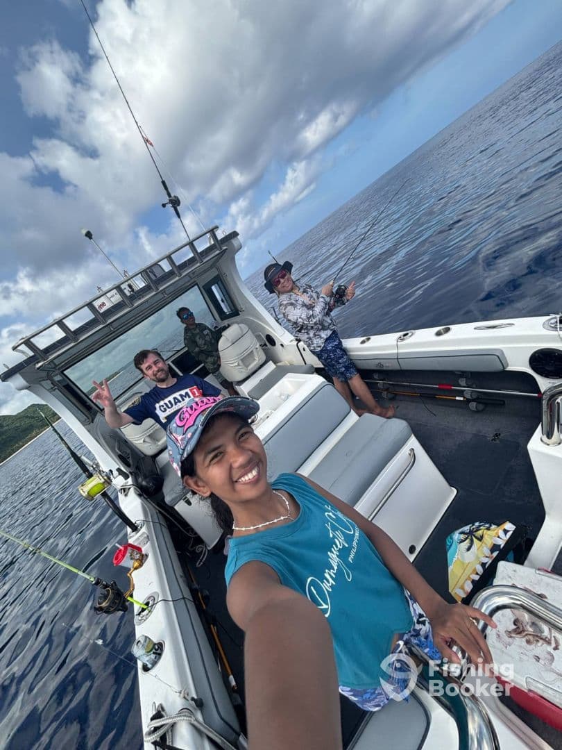 A young angler smiling while taking a selfie on a fishing boat, with friends in the background enjoying a day of fishing in open waters.
