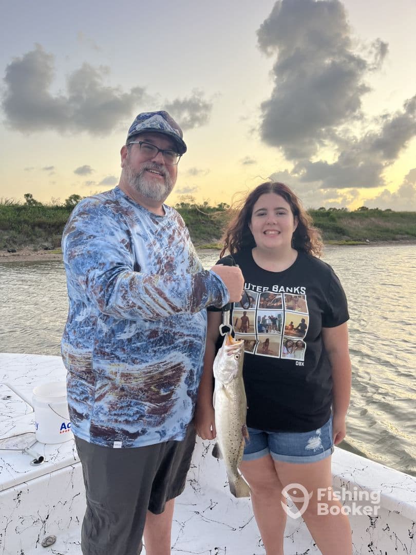 A proud father and daughter duo displaying a large Speckled Trout while enjoying a fishing trip on the water.