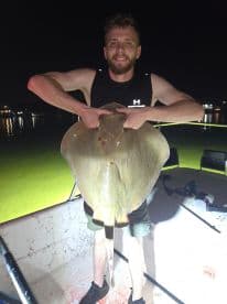 Angler proudly displaying a large stingray caught during a night fishing trip, showcasing the excitement of fishing under the stars.