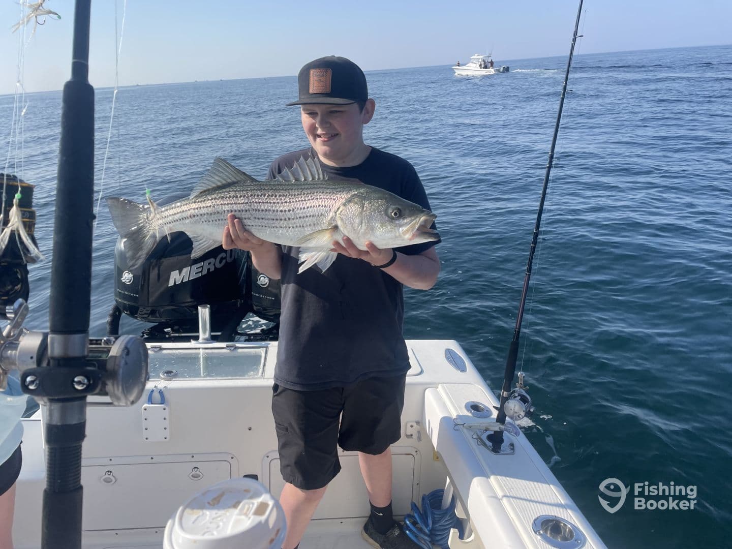 A young angler proudly displaying a large Striped Bass while fishing on a boat in open waters.