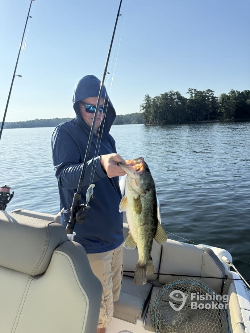 A young angler proudly displaying a large Largemouth Bass while fishing on a serene lake, showcasing a beautiful morning fishing environment.