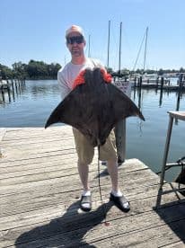 Angler proudly displaying a large stingray caught at the dock, showcasing a sunny day on the water.