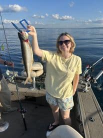 An angler proudly displaying a large Lake Trout while fishing on a calm lake, showcasing a beautiful summer day.
