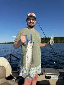 Angler proudly displaying a large Lake Trout while fishing on a boat in a serene lake setting.