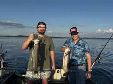 Two anglers proudly displaying their catches of Lake Trout while fishing on a calm lake, showcasing a beautiful day on the water.