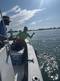 Two anglers enjoying a sunny day on the water, with one actively reeling in a catch while the other assists on a small fishing boat.