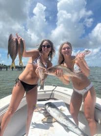 Two anglers proudly displaying their catch of Snapper and other fish on a sunny day aboard a boat.