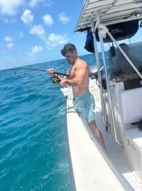 A solo angler reeling in a catch while fishing from a center console boat in clear blue waters.