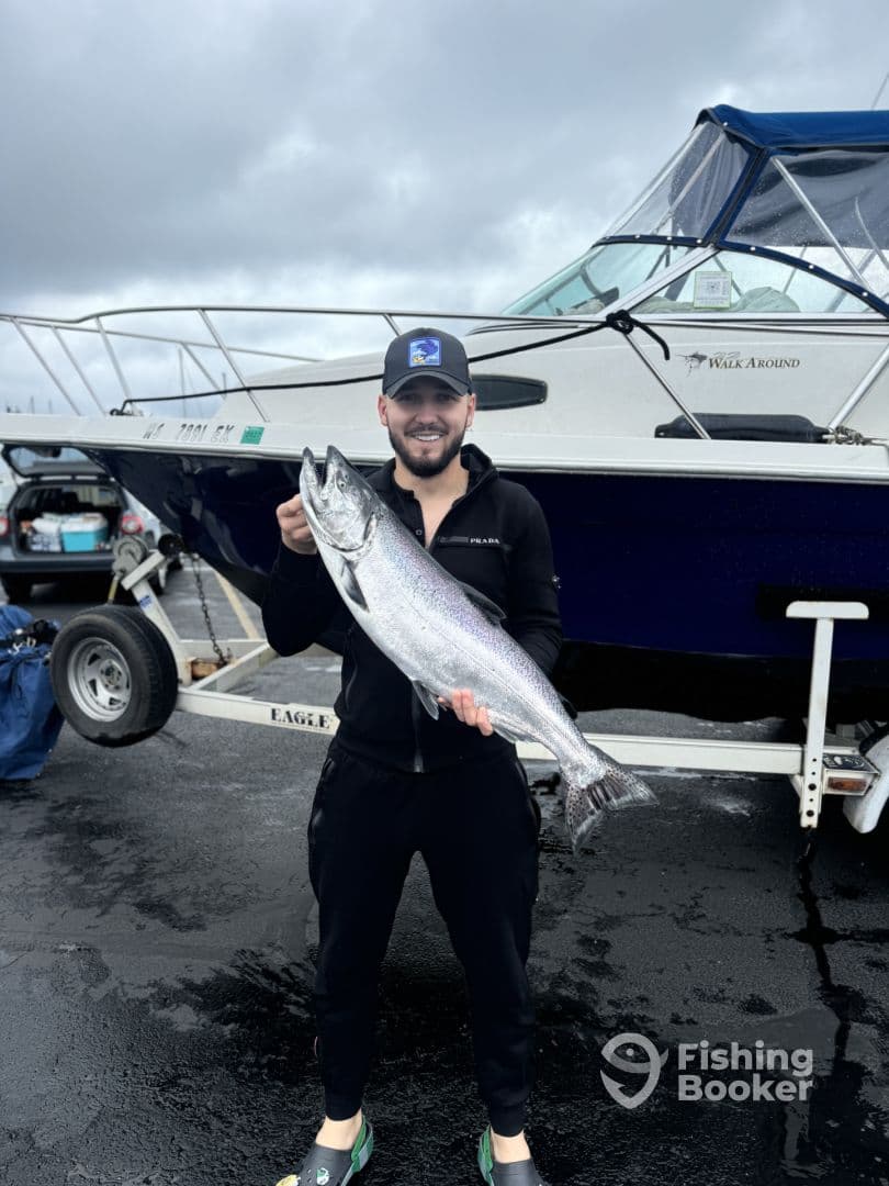 Angler proudly displaying a large Salmon at the dock, with a fishing boat in the background, showcasing a successful fishing trip.