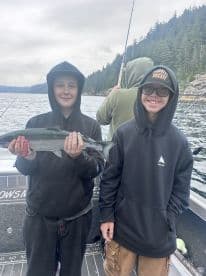 Two young anglers proudly displaying a caught fish while fishing in a scenic coastal environment.