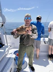 Angler proudly displaying a large Grouper while fishing on a charter boat in open waters.