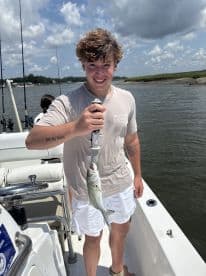 A young angler proudly displaying a caught fish while aboard a fishing boat in a scenic waterway.