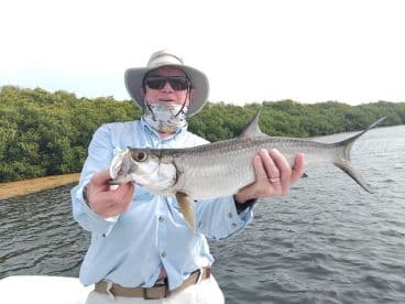 An angler proudly displaying a Silver Tarpon caught during a fishing trip in a mangrove-lined waterway.