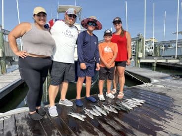 A family poses proudly at the dock with their catch of speckled trout after a successful fishing trip.