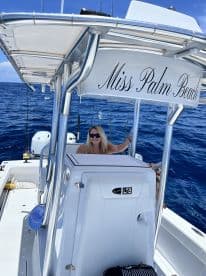 A woman enjoying the helm of the 'Miss Palm Beach' boat, surrounded by the deep blue ocean, showcasing the boat's interior features.