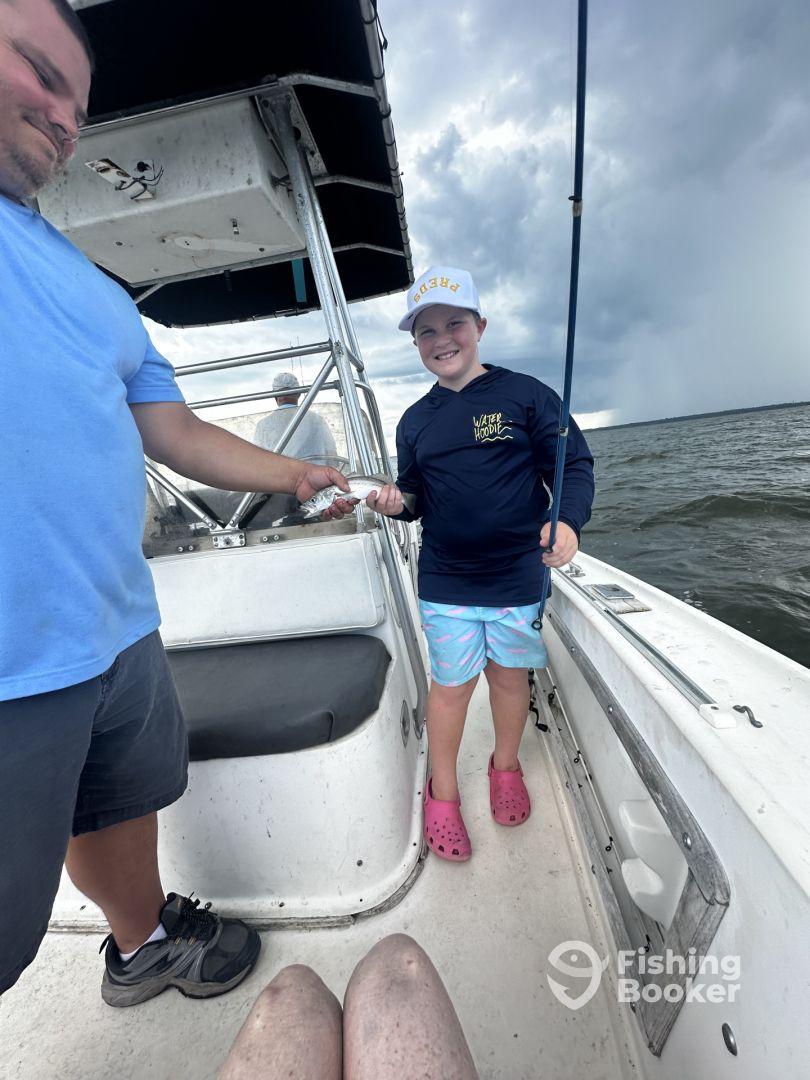 A young angler smiling while holding a small fish on a boat, showcasing a fun fishing experience with family.
