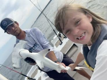 A young angler and an adult proudly displaying a caught shark while fishing on a boat, showcasing a fun family fishing experience.