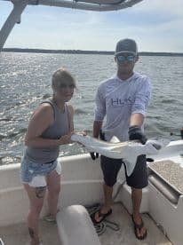 Two anglers proudly displaying a caught shark while on a boat, enjoying a day of fishing in a scenic waterway.