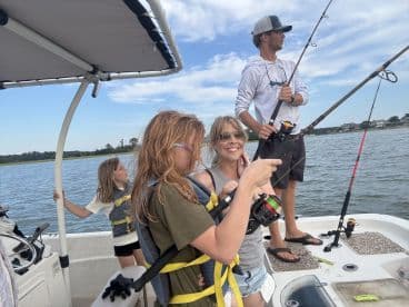 A family enjoying a fishing trip on a boat, with children actively engaged in fishing while the scenic waterway is visible in the background.