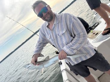 An angler proudly displaying a caught shark while fishing on a boat, showcasing a successful day on the water.