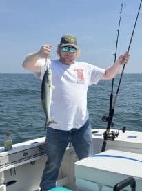 Angler proudly displaying a Bluefish while fishing on a boat in open waters.