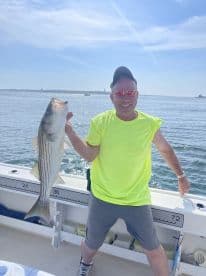 An angler proudly displaying a large Striped Bass while fishing on a sunny day, showcasing the excitement of a successful catch.