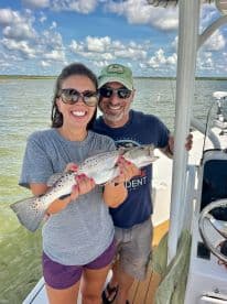 Two anglers proudly displaying a Speckled Trout while enjoying a day on the water, showcasing a fun fishing experience.