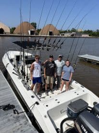 Group of four anglers posing on the deck of a fishing boat, showcasing multiple fishing rods in a scenic marina setting.