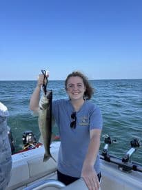 A young woman proudly displaying a freshly caught Walleye while fishing on a boat in open waters.
