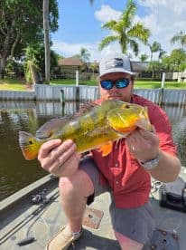 Angler proudly displaying a vibrant Peacock Bass while fishing from a boat in a scenic waterway.