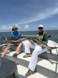 Two anglers proudly displaying their catches of Cobia while enjoying a sunny day on the water.