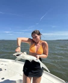 A young woman proudly displaying a caught shark while enjoying a sunny day on the water.